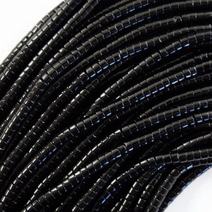 Op de afbeelding: Een streng zwarte, gefacetteerde, ronde kralen. De kralen zijn klein en uniform van grootte. De streng is opgerold en in een patroon gerangschikt.