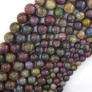 Può includere: Una collana di perle rotonde in pietre preziose multicolori. Le perle sono un mix di marrone, rosa, verde e blu. Le perle sono tutte più o meno della stessa dimensione e sono infilate su un filo rosso.