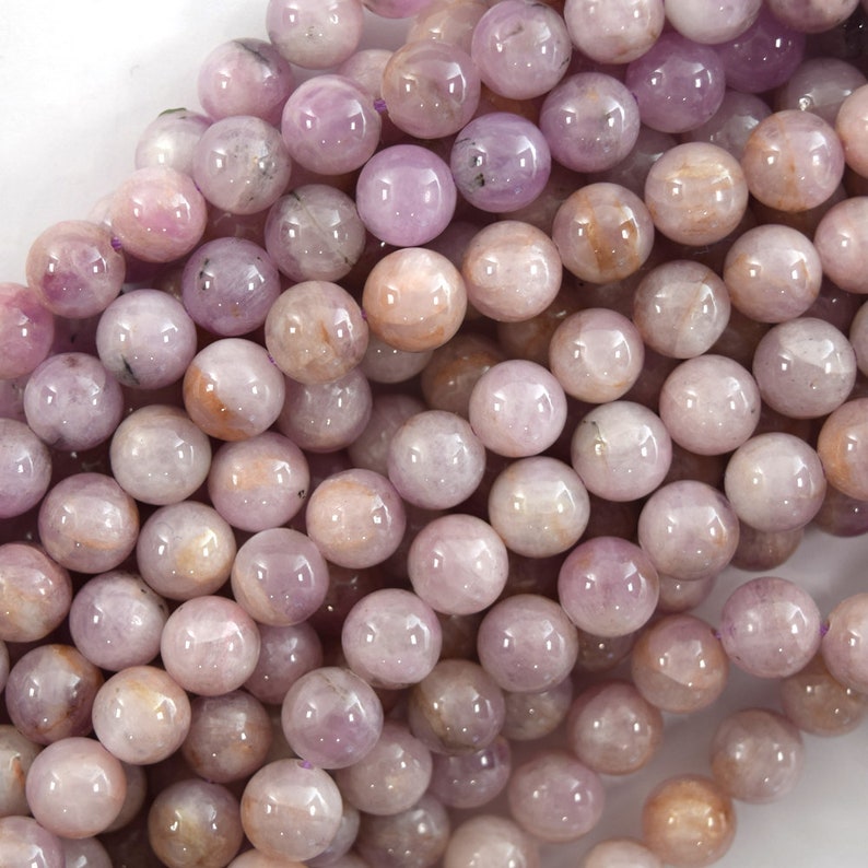 May include: A strand of round, smooth, purple and pink gemstone beads. The beads have a slightly iridescent sheen.