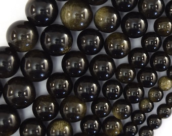 Puede incluir: Una colección de cuentas redondas y pulidas de varios tamaños, con un color base negro profundo y sutiles inclusiones de color marrón dorado brillante en la superficie de cada cuenta de piedra, dispuestas en un grupo denso y superpuesto.