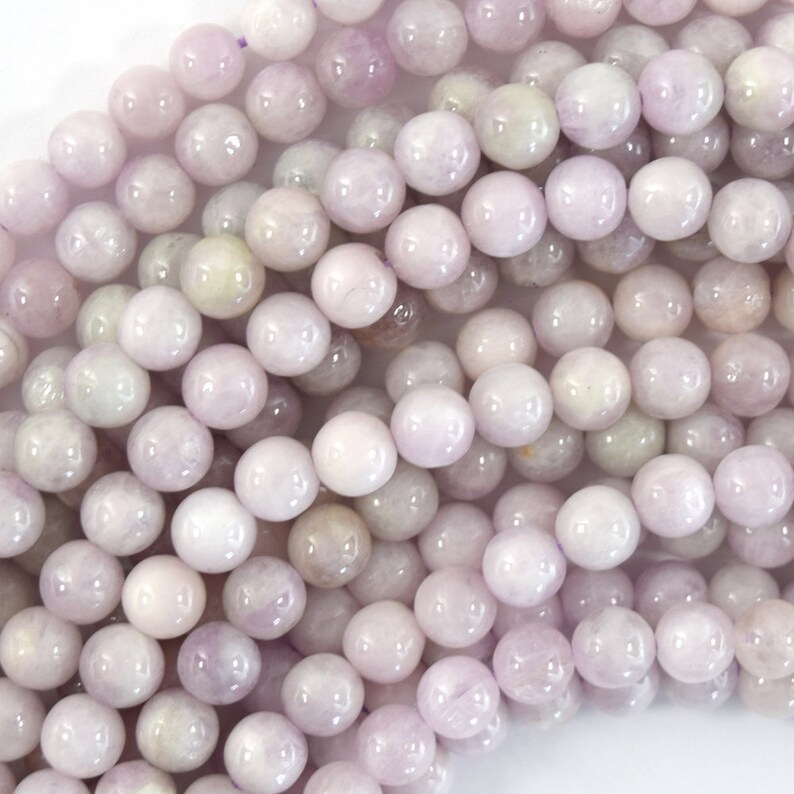 May include: A strand of pale lavender round gemstone beads. The beads are smooth and polished, with a subtle shimmer.