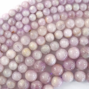 May include: A strand of pale lavender round gemstone beads. The beads are smooth and polished, with a slight shimmer.
