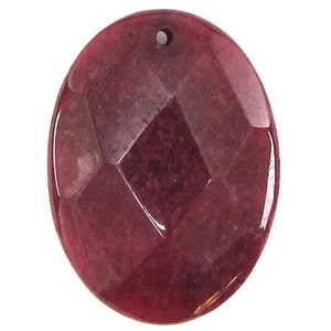 May include: A deep red oval-shaped gemstone pendant with a faceted design. The pendant has a hole at the top for stringing.