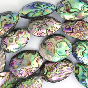 May include: A collection of iridescent abalone shell beads in various shades of green, blue, and purple. The beads are oval shaped and have a smooth, polished surface.