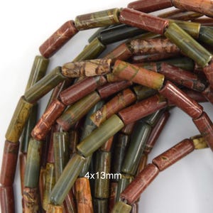 May include: A collection of cylindrical beads made of natural stone in shades of olive green, reddish-brown, and tan with marbled patterns. Each bead measures 4x13mm. The beads are arranged in a loose pile, showing varied textures and earthy tones.