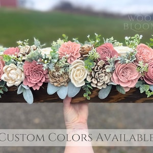May include: A wooden box filled with a floral arrangement of sola wood flowers in shades of blush pink, cream, and beige. The flowers are arranged in a rustic style and include roses, peonies, and other blooms. The box is stained a dark brown color and has a distressed finish. The text "WOOD BLOOMS" is visible in the upper right corner of the image. The text "CUSTOM COLORS AVAILABLE" is visible at the bottom of the image.