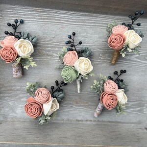May include: Five small bouquets of artificial flowers in shades of pink, white, and green. Each bouquet is made with felt flowers and greenery, and is attached to a small piece of burlap.
