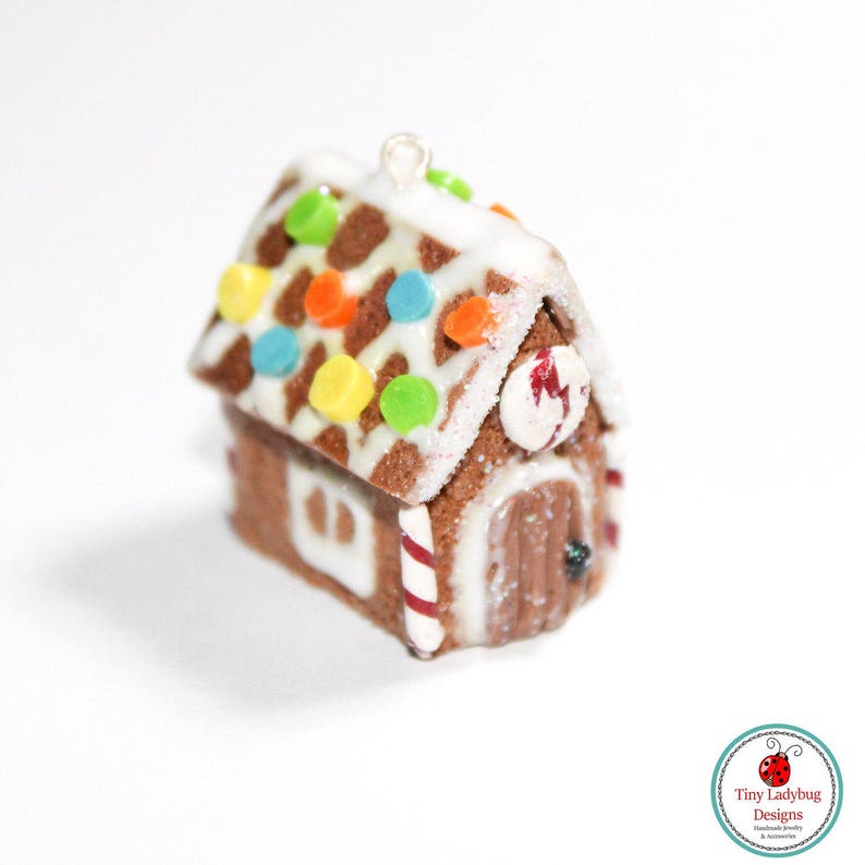 May include: A miniature gingerbread house ornament with a brown base, white icing, and colorful candy decorations. The roof features brown spots and colorful round candies. The door has a red and white candy cane stripe.