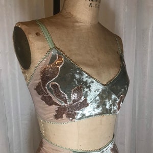 May include: A two-piece lingerie set with a sage green velvet fabric and delicate floral embroidery. The set features a bralette with adjustable straps and a matching high-waisted bottom.