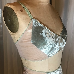 May include: A lingerie set with a green and beige velvet fabric. The top has a sweetheart neckline and the bottom is a high-waisted skirt.