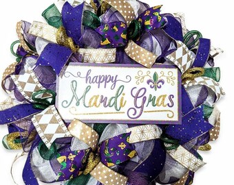 Puede incluir: Una corona de Mardi Gras de color morado, verde, dorado y blanco con un letrero que dice "happy Mardi Gras".