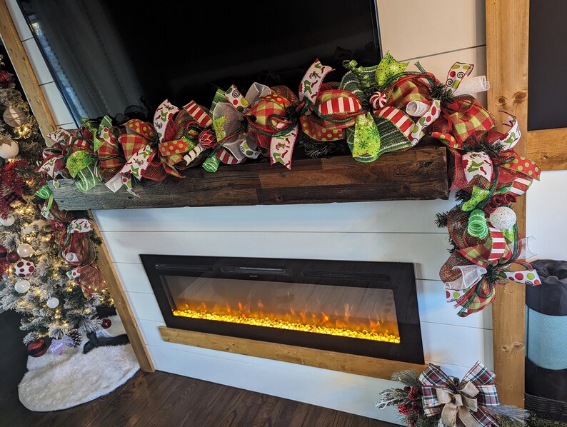 May include: A festive Christmas garland with red, green, and white bows and ribbons, decorated with candy canes and other holiday accents. The garland is draped over a wooden mantel above a fireplace.