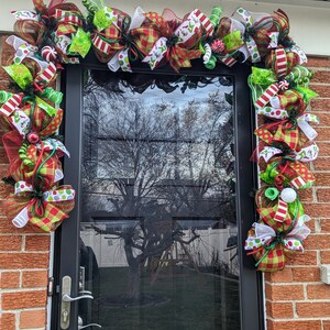 May include: A Christmas door wreath with red, green, and white bows, candy canes, and polka dots. The wreath is decorated with a variety of festive elements, including bows, ribbons, and candy canes.