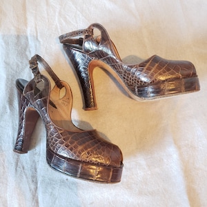 May include: A pair of brown leather platform heels with a peep toe and ankle strap. The heels are made of a textured material that resembles crocodile skin.