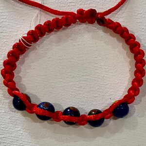 May include: Red string bracelet with blue and gold beads. The price tag says "$3.50".