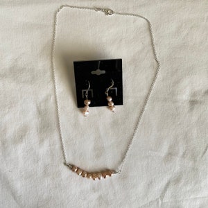 May include: A silver chain necklace with a row of pink pearls and matching pink pearl drop earrings.