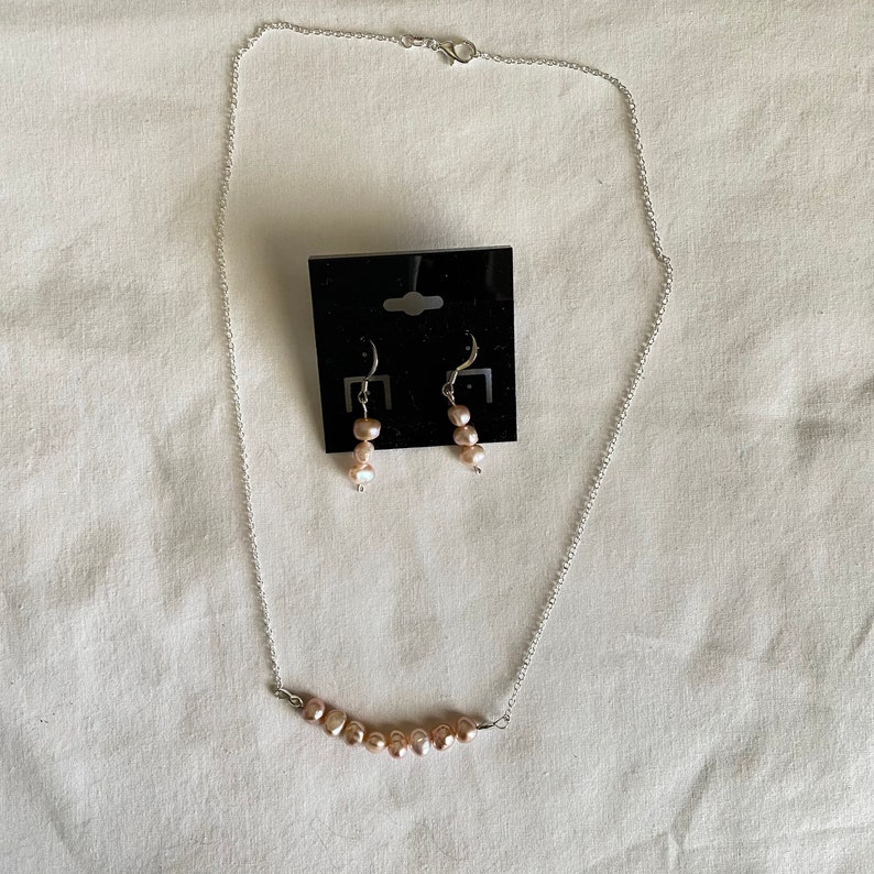 May include: A silver chain necklace with a row of pink pearls and matching pink pearl drop earrings.