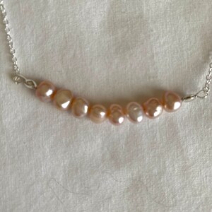 May include: A delicate silver chain necklace with a row of seven pale pink pearls.