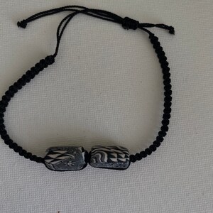 May include: A black cord bracelet with two black and white patterned cylindrical beads.