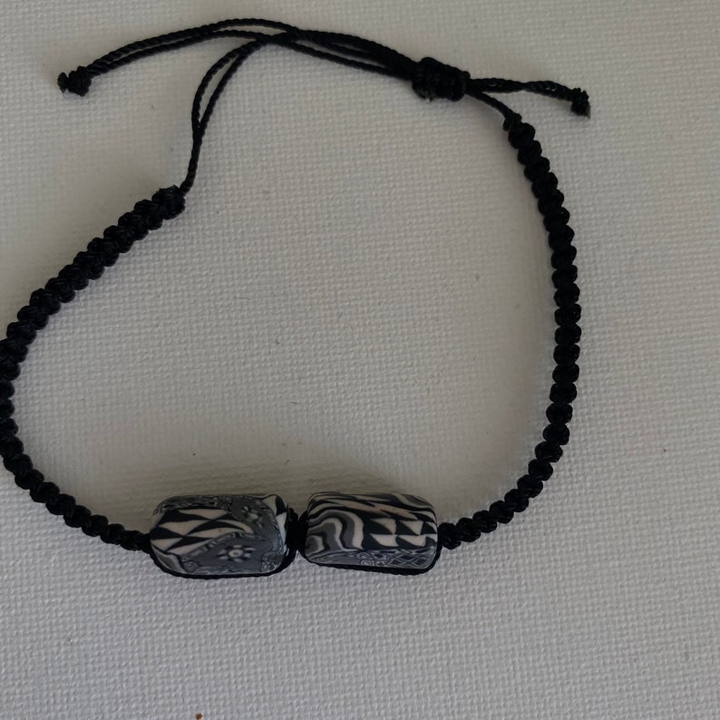 May include: A black cord bracelet with two black and white patterned cylindrical beads.