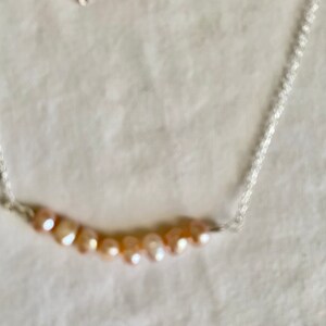 May include: A silver chain necklace with a row of light pink and peach colored pearls.