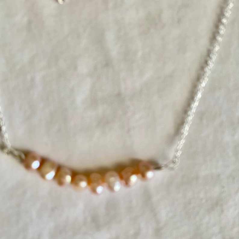 May include: A silver chain necklace with a row of light pink and peach colored pearls.