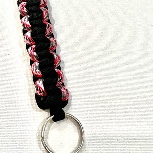 K&ouml;nnte beinhalten: Ein schwarzer und pinkfarbener Paracord-Schl&uuml;sselanh&auml;nger mit einem silbernen Schl&uuml;sselring.
