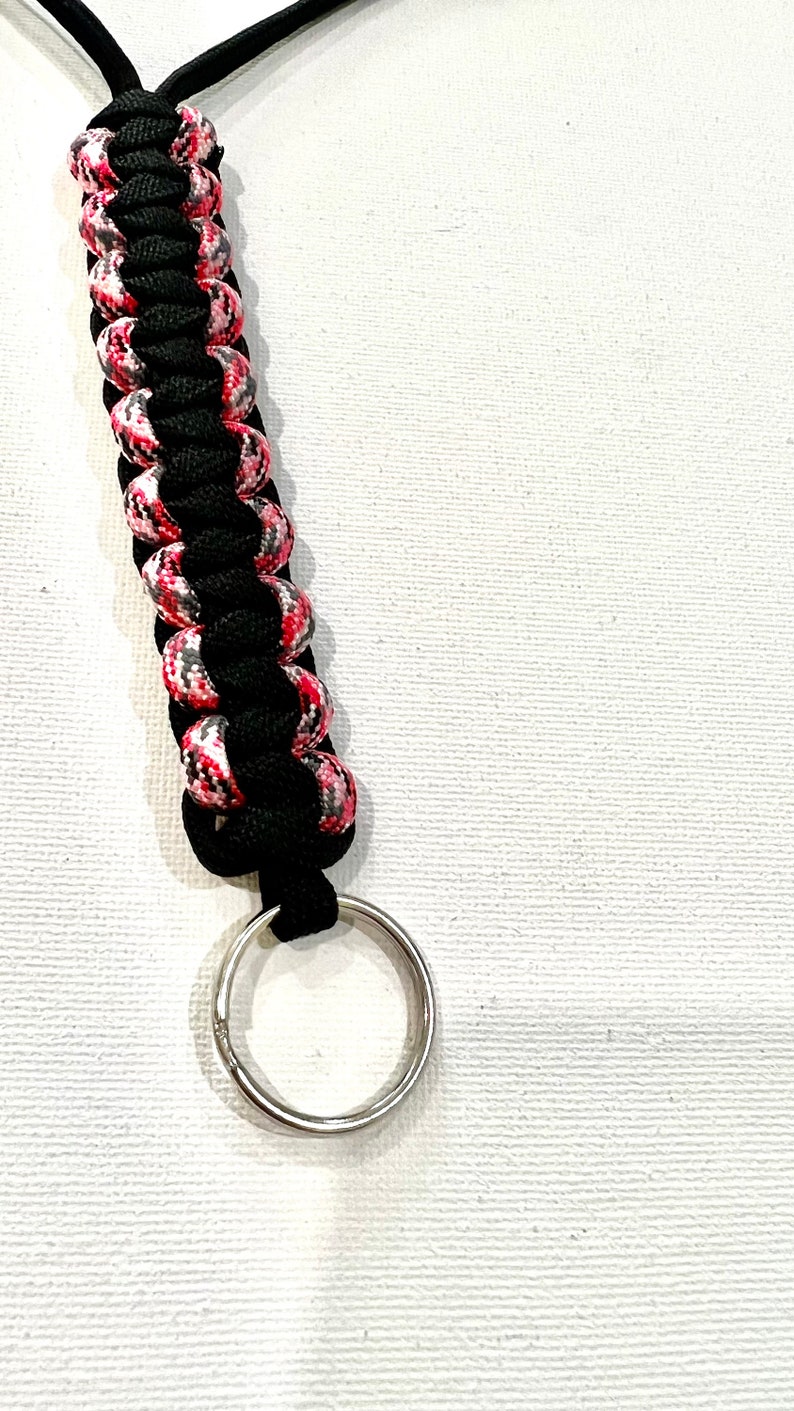 K&ouml;nnte beinhalten: Ein schwarzer und pinkfarbener Paracord-Schl&uuml;sselanh&auml;nger mit einem silbernen Schl&uuml;sselring.