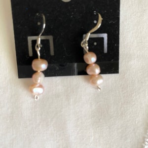 May include: A pair of silver earrings with three pink pearls on each earring.