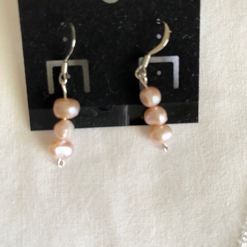 May include: A pair of silver earrings with three pink pearls on each earring.