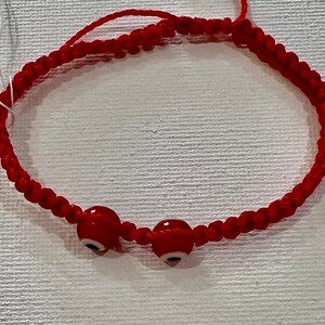 May include: Red string bracelet with three red evil eye beads. The bracelet is tied with a knot.