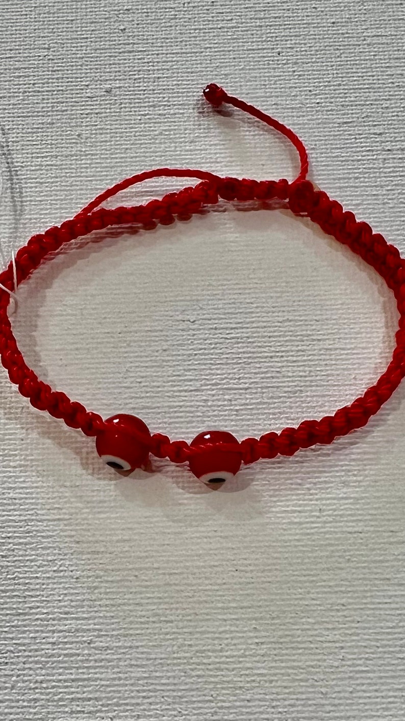 May include: Red string bracelet with three red evil eye beads. The bracelet is tied with a knot.