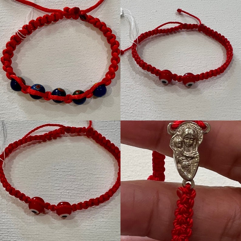 May include: Three red string bracelets with different charms. The first bracelet has blue and white glass beads. The second bracelet has two red evil eye beads. The third bracelet has a silver charm of the Virgin Mary and baby Jesus.