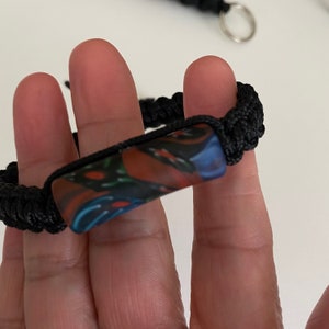 May include: A black paracord bracelet with a colorful, abstract patterned bead.