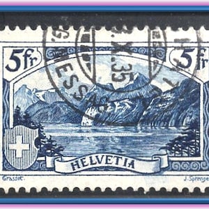 Op de afbeelding: Een blauw-witte postzegel met een bergmeerlandschap met het woord "HELVETIA" op een banner. De postzegel heeft een waarde van 5fr en een Zwitsers kruis-embleem. De postzegel is omlijst door een blauwe rand.