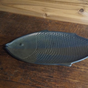May include: A dark blue ceramic fish-shaped serving dish. The dish has a textured surface that resembles fish scales.