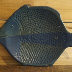 May include: A blue and green ceramic fish-shaped dish with a textured surface. The dish is designed to look like a fish with scales and a fin.