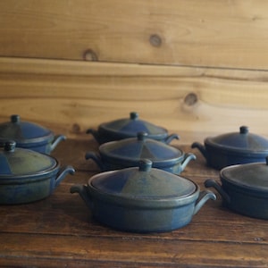 May include: Eight blue and green ceramic serving dishes with lids. The dishes are arranged in two rows of four on a wooden surface.
