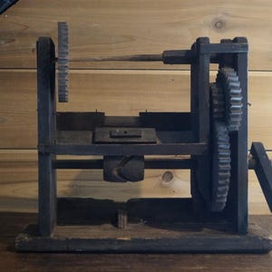 May include: A vintage wooden machine with gears and a metal rod. The machine is made of dark wood and has a rustic appearance.