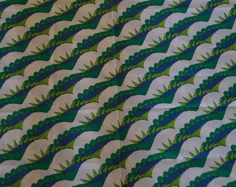 May include: White fabric with a repeating pattern of green and blue stylized flower shapes. The flowers are arranged in a wave-like pattern.