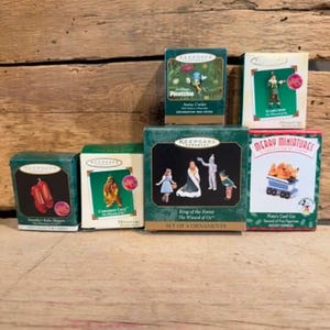 May include: A collection of six Hallmark Keepsake miniature ornament boxes featuring characters from The Wizard of Oz, Pinocchio, and Disney. The boxes display illustrations of Dorothy's Ruby Slippers, the Cowardly Lion, Jiminy Cricket, the Scarecrow, a four-piece set of Wizard of Oz figures, and Pluto in a coal car.