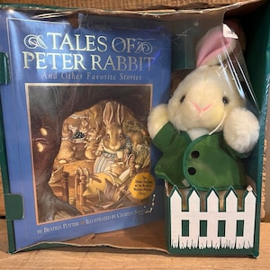 May include: A green and white plush Peter Rabbit toy with a green jacket and a white picket fence. The toy is packaged with a book titled "The Complete Tales of Peter Rabbit and Other Favorite Stories" by Beatrix Potter.