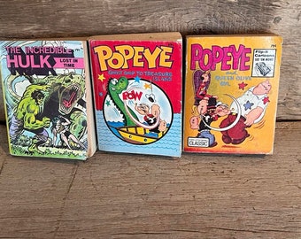 May include: Three vintage comic books featuring the Incredible Hulk, Popeye, and Popeye. The Incredible Hulk comic book features a green Hulk fighting a dinosaur. The Popeye comic books feature Popeye and Olive Oyl in various scenes.