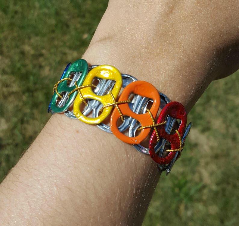May include: A rainbow colored bracelet made from recycled aluminum pull tabs. The bracelet is made of six pull tabs, each painted a different color of the rainbow. The pull tabs are connected together with wire.