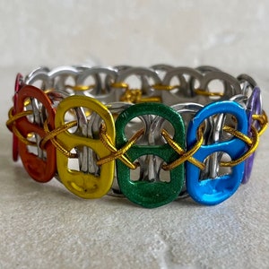 May include: A rainbow colored bracelet made from pull tabs connected with gold cord.
