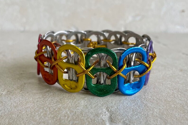May include: A rainbow colored bracelet made from pull tabs connected with gold cord.