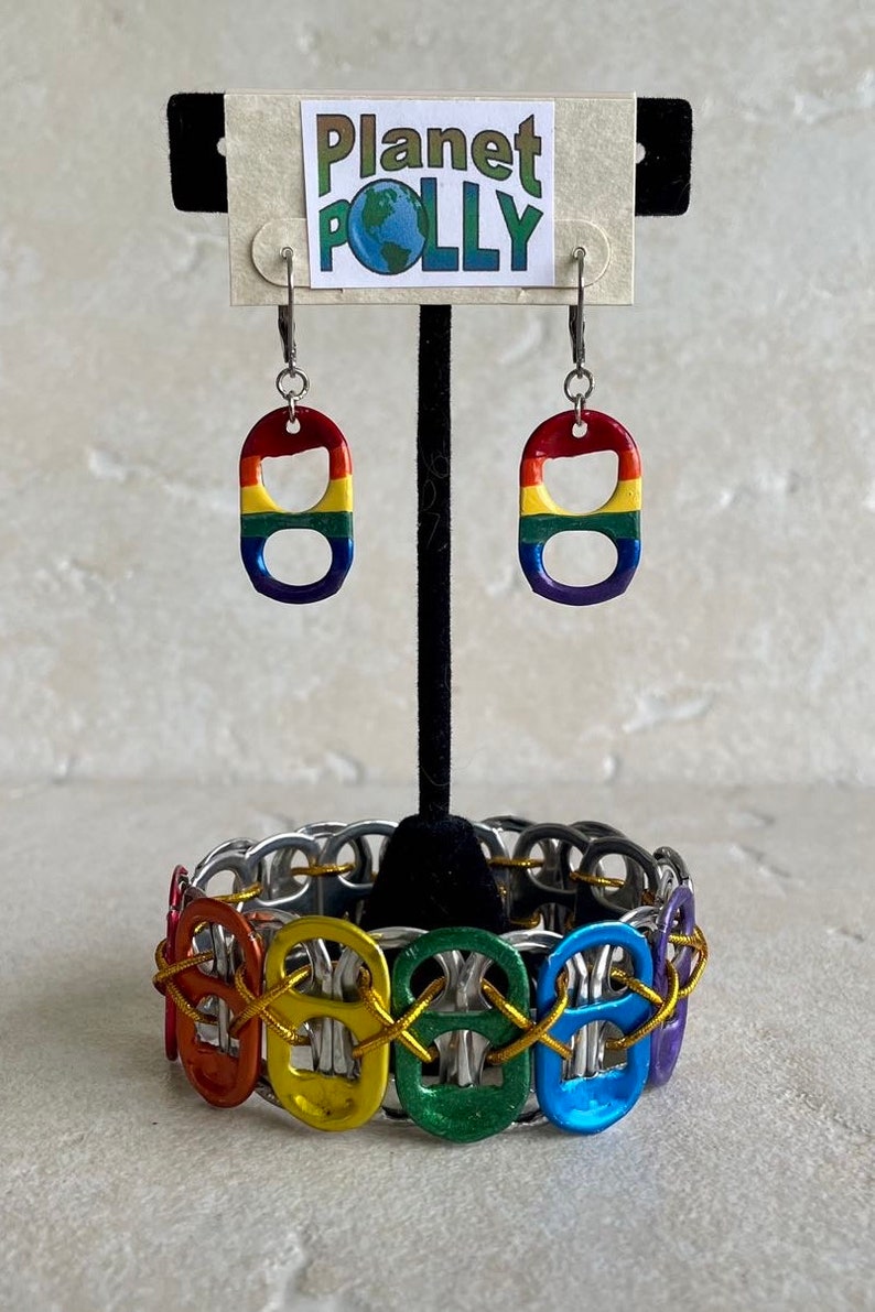 May include: Rainbow colored pull tab earrings and a bracelet made from pull tabs. The earrings are hanging from a display card that says "Planet Polly".