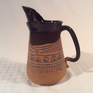 May include: A brown and black ceramic jug with a geometric design. The jug has a wide mouth and a handle.