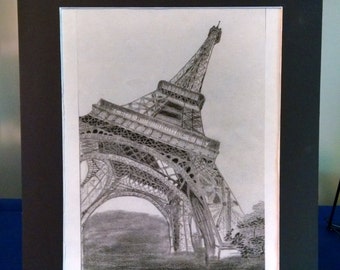 May include: A black and white pencil drawing of the Eiffel Tower in Paris, France. The drawing is framed in a black frame.