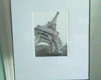 May include: A framed black and white drawing of the Eiffel Tower in Paris, France. The drawing is in a simple black frame and is displayed on an easel.